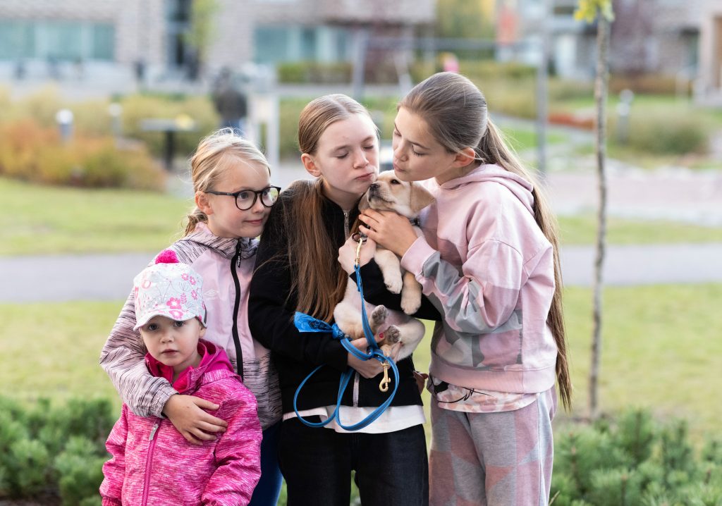 Neljä nuorta lasta ulkona. Yhdellä lapsella on sylissään koira.