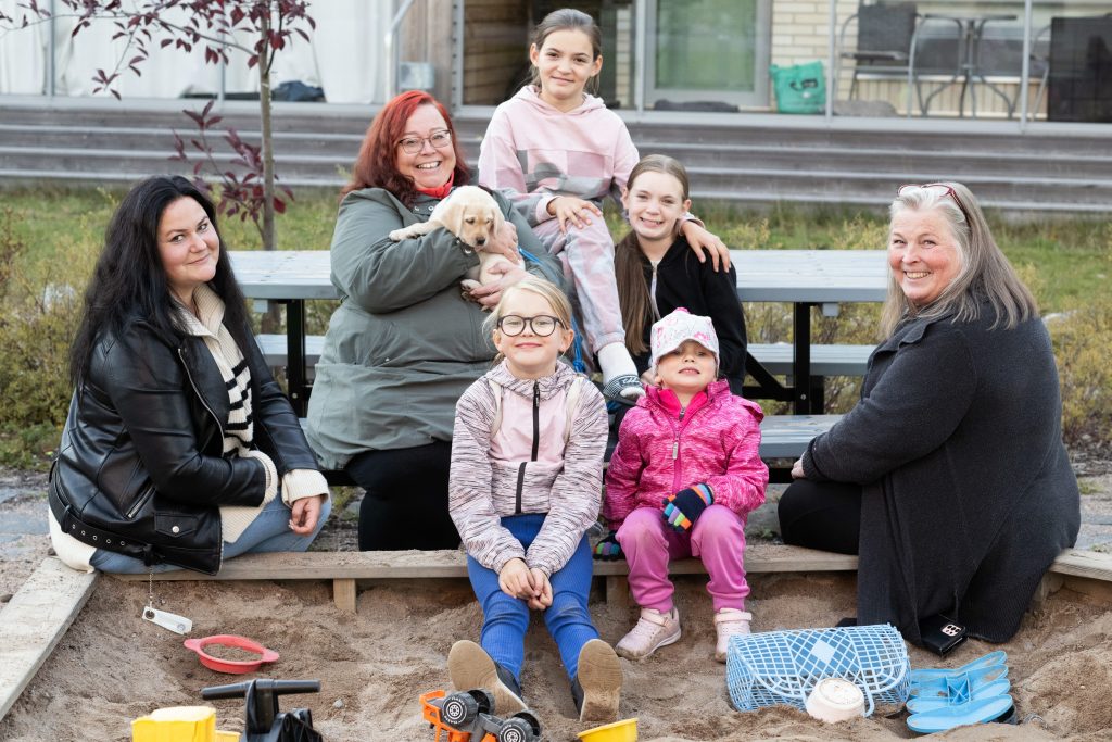 Vuoden asukastoimikunta lapsineen istuu hiekkalaatikon ääressä.